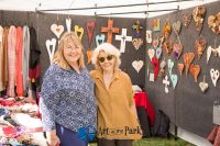 Art in the Park 2021 smiling women in booth with cross and heart art